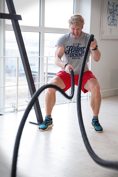 Mann trainiert mit schwarzem Battle Rope in hellem Fitnessraum